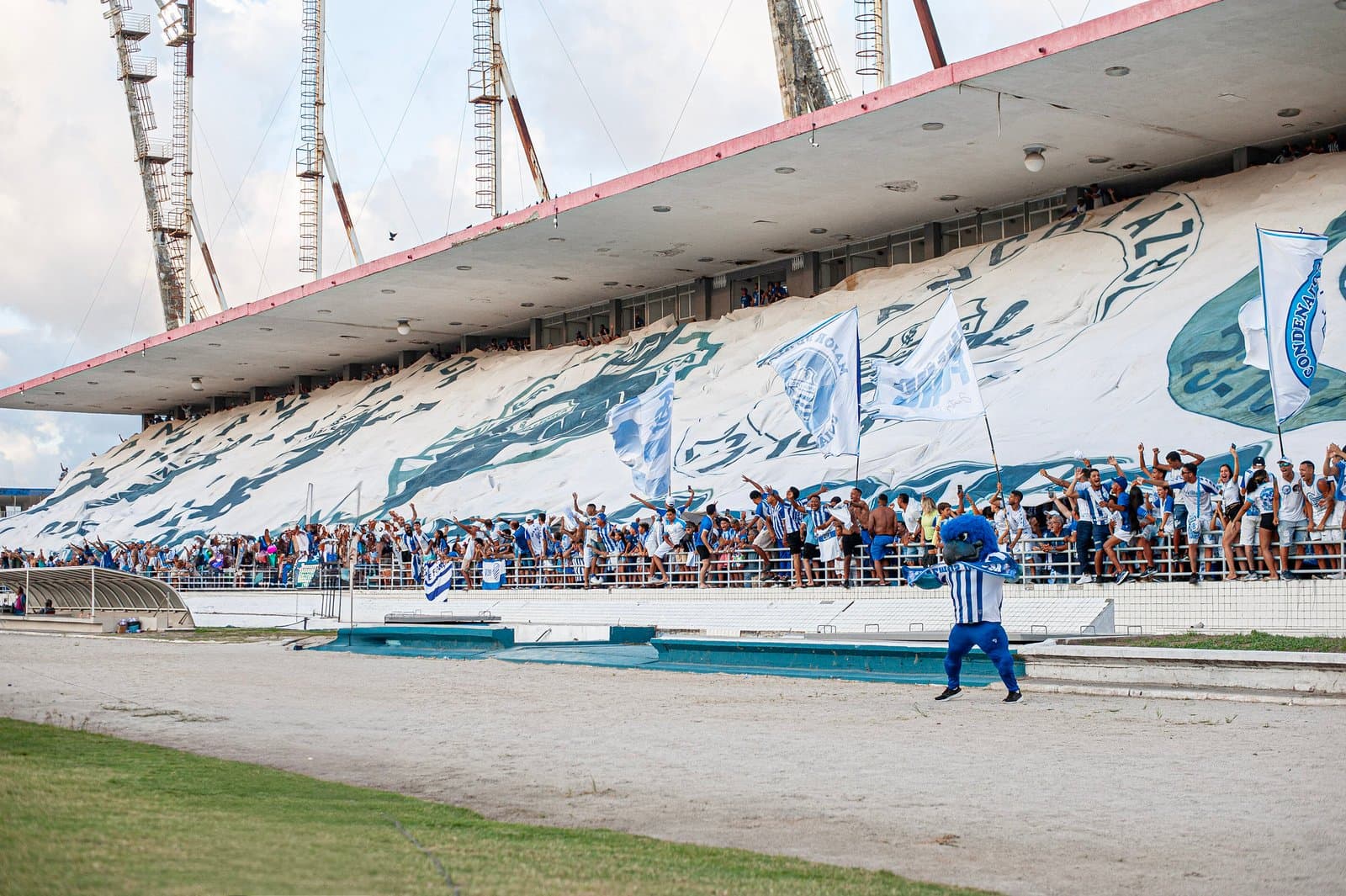 Torcida Mancha Azul do CSA faz festa no Estádio Rei Pelé com bandeiras e faixas durante jogo em Maceió.