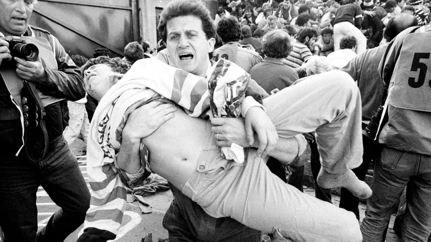 Homem carrega vítima durante a tragédia de Heysel em 1985, na final da Champions entre Juventus e Liverpool, em Bruxelas.