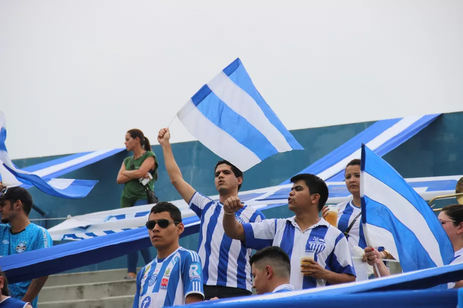 Torcida do São Raimundo-RR com bandeiras azul e branco apoiando o time em jogo fora dos grandes centros do futebol brasileiro.